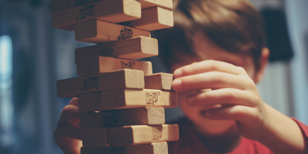 A boy carefully sliding out a block from a Jenga tower